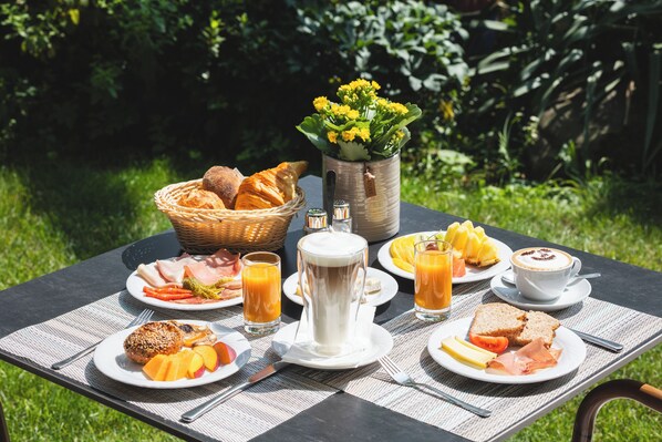 A breakfast table set outdoors with plates of food, a coffee pot, and a basket of bread.