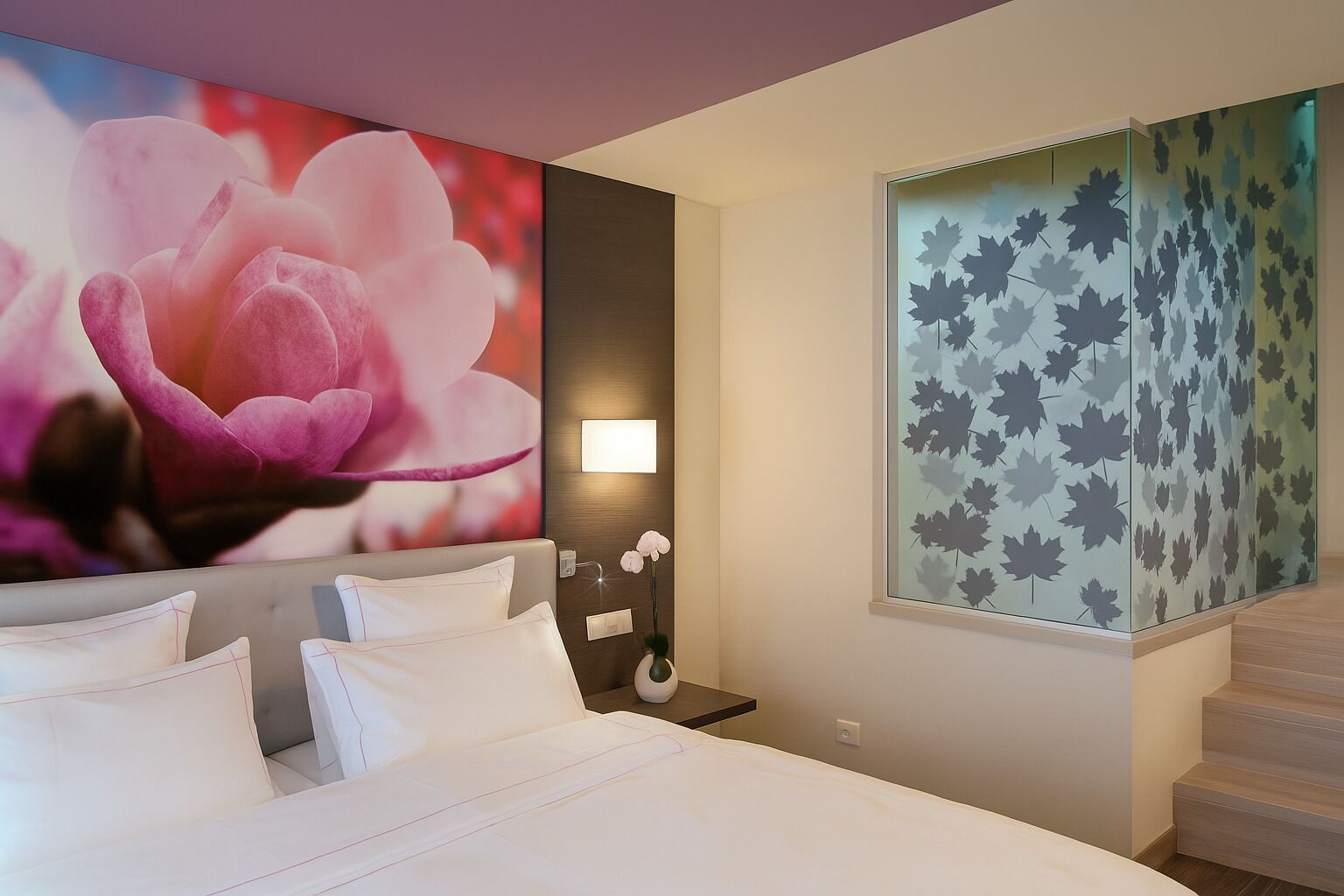 A hotel room with a large bed, a wall-mounted lamp, a nightstand, and a window with a leaf pattern.