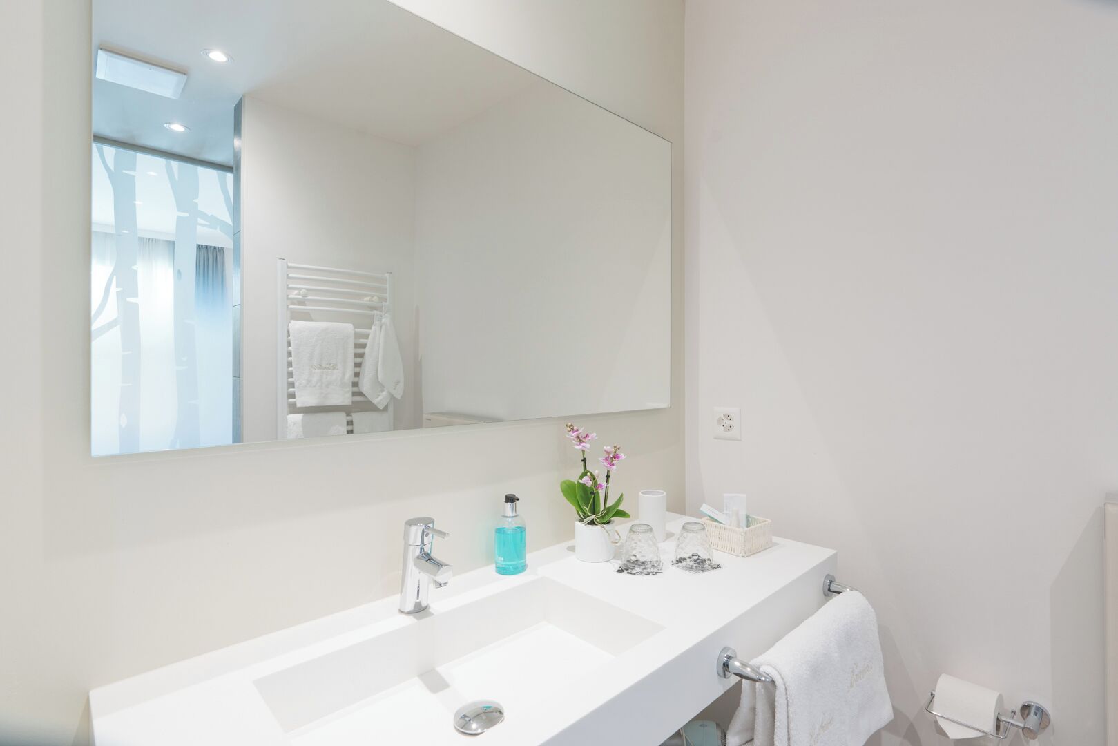 Un baño moderno con un espejo grande, lavamanos blanco y un perchero para toallas.