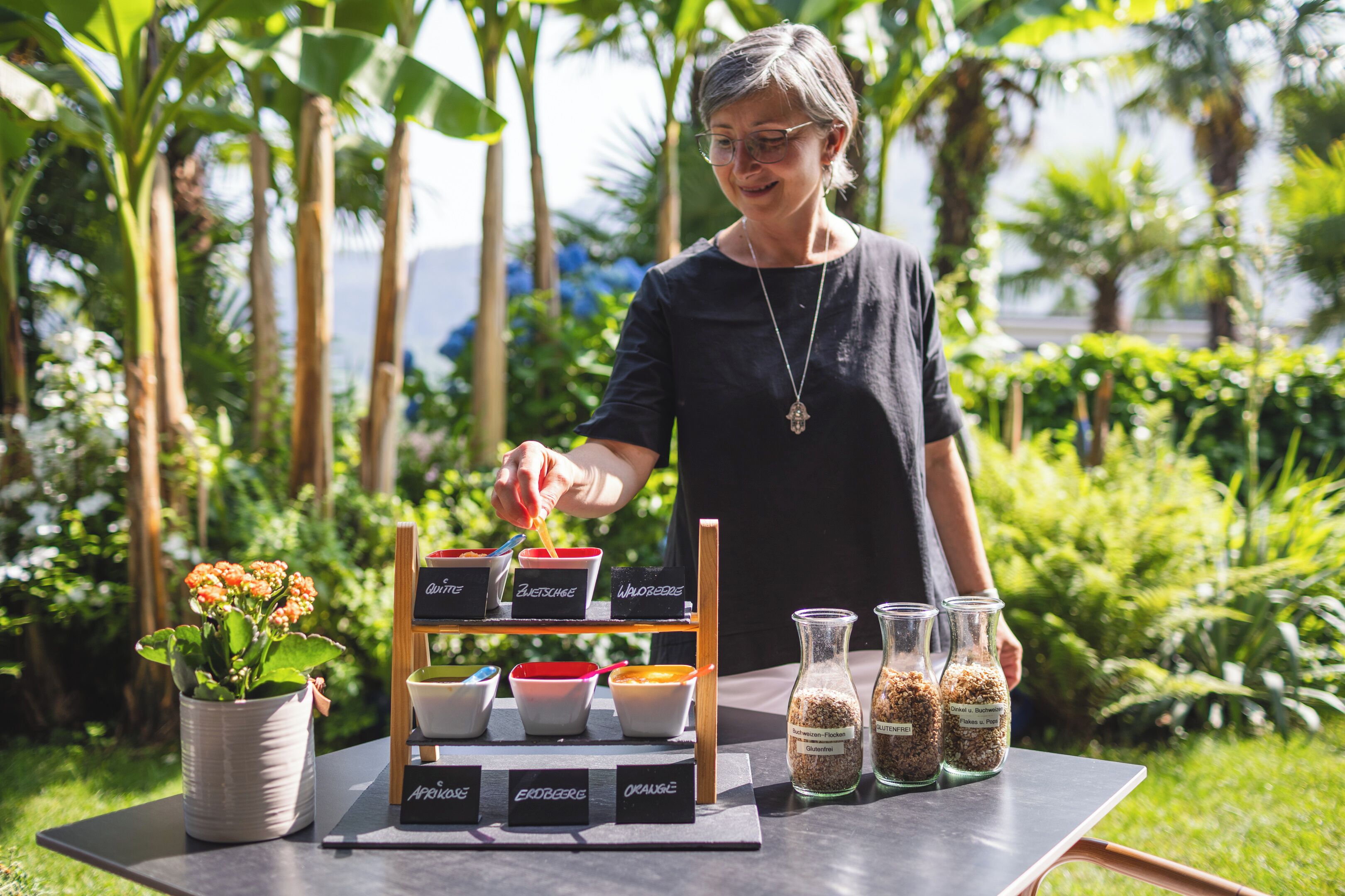 A person arranging food items on a table outdoors with a garden background.