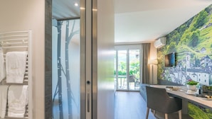 Un baño moderno con cabina de ducha de vidrio, un perchero con toallas blancas y vistas a un balcón con mesa y sillas.