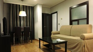 Een moderne woonkamer met een bank, salontafel, televisie en een eethoek met stoelen en een lamp.