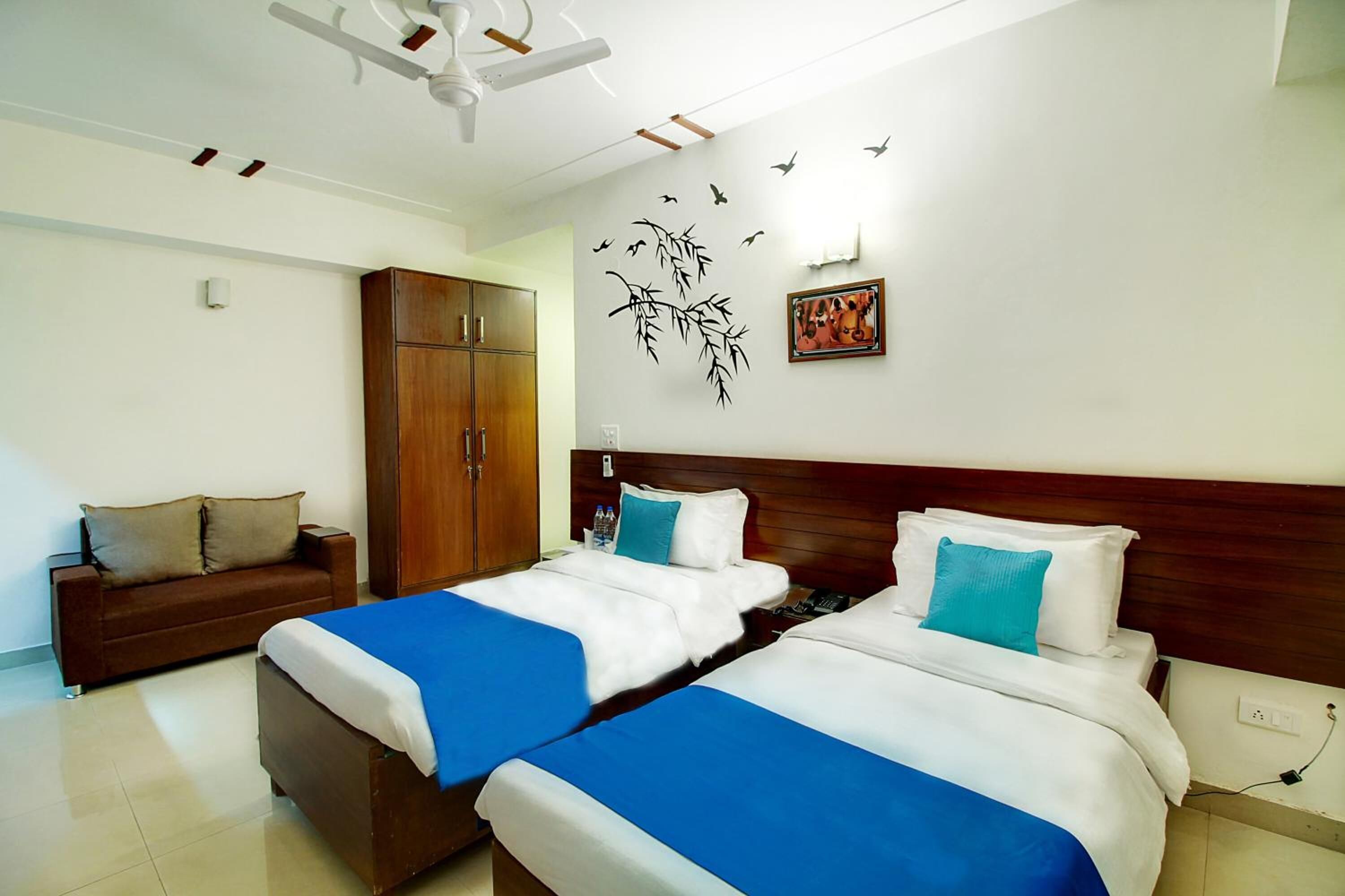 A hotel room with two beds, a wooden wardrobe, a sofa, and decorative wall art.