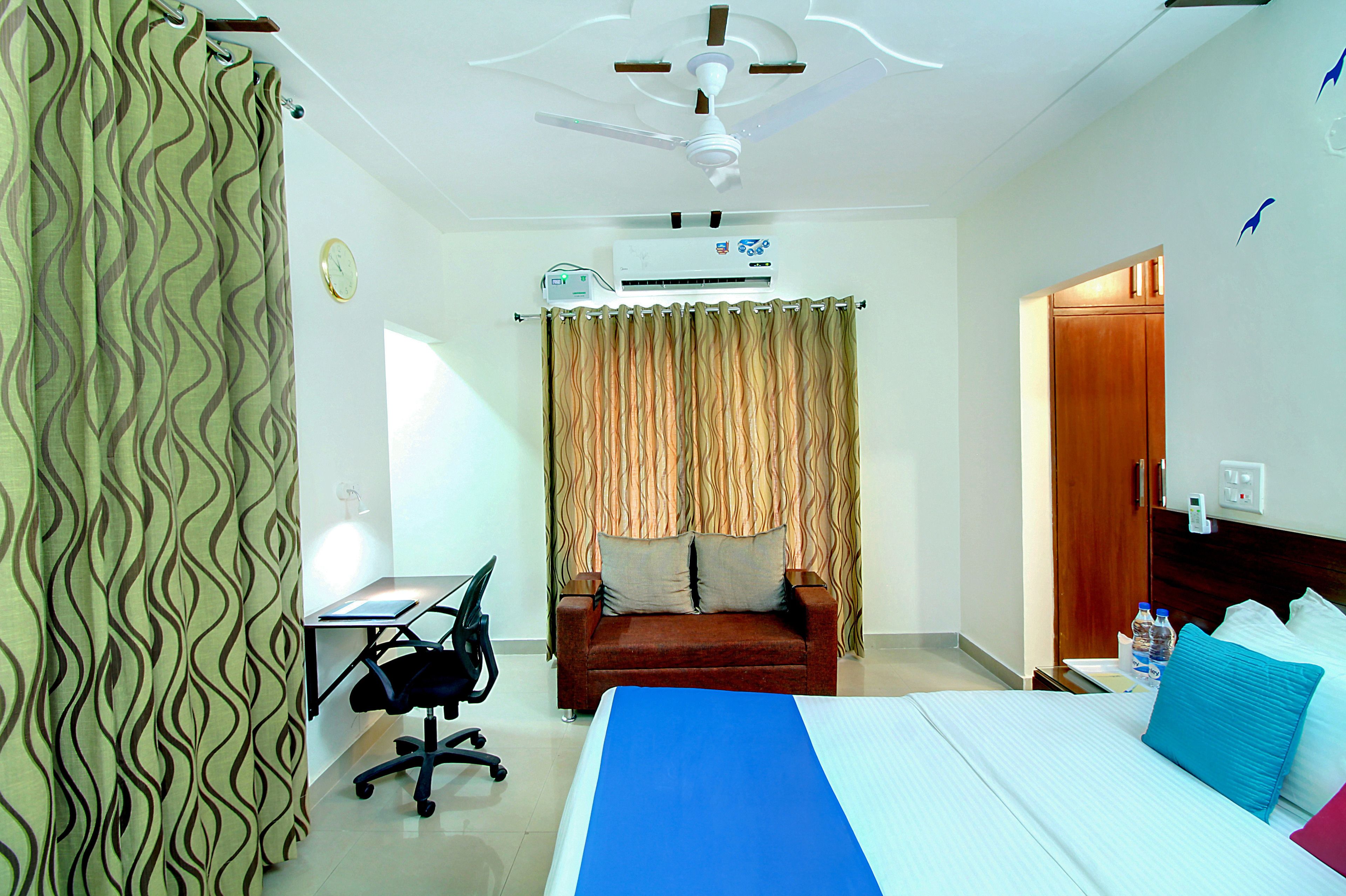 Habitación de hotel con cama, escritorio, silla, sofá, ventilador de techo y aire acondicionado.
