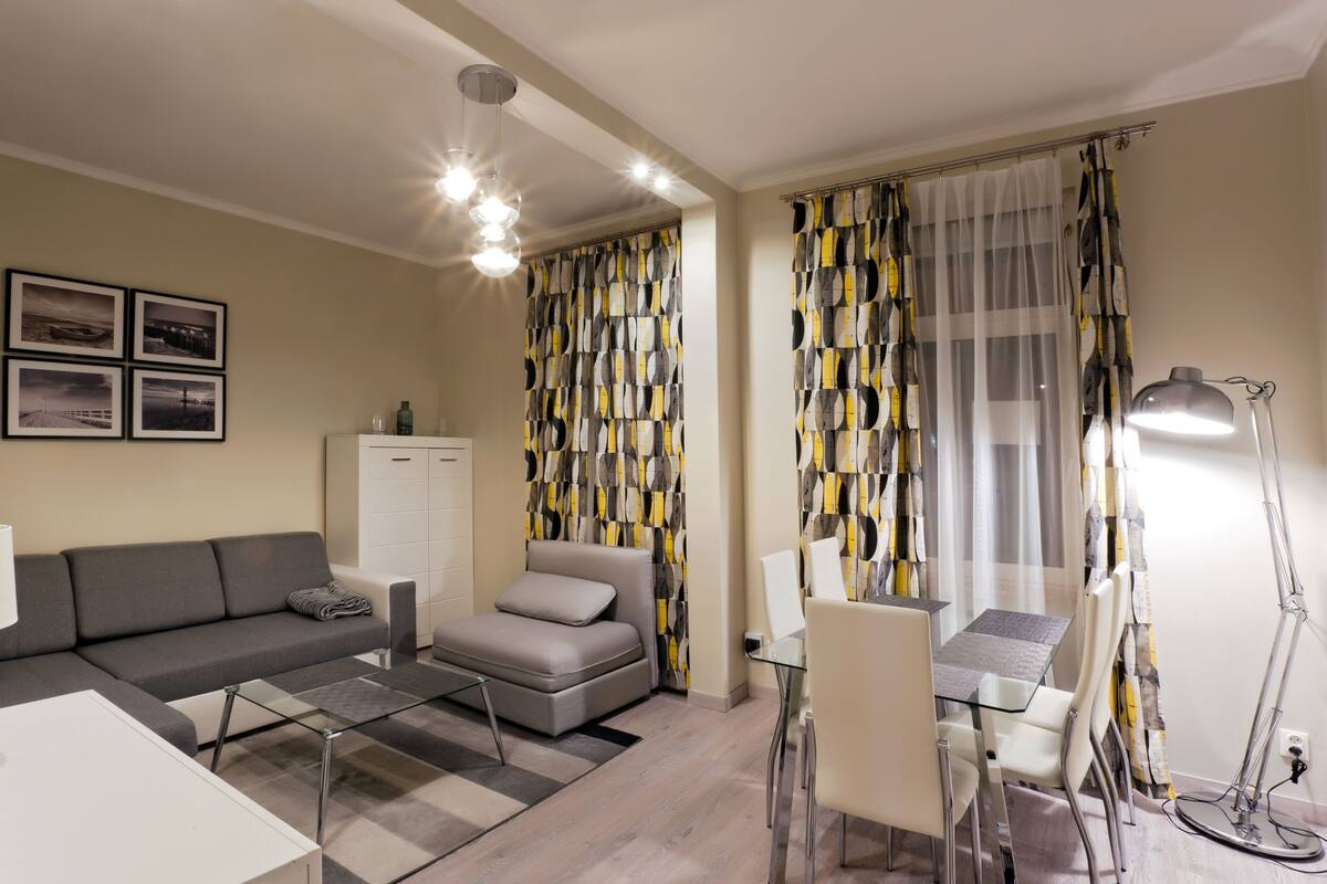 A modern living room with a sofa, a small table, a glass coffee table, and a dining area with chairs.