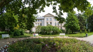 A large building with a symmetrical facade, surrounded by lush greenery and a well-maintained garden with benches. - Apartments Happy Hours (Sopot)