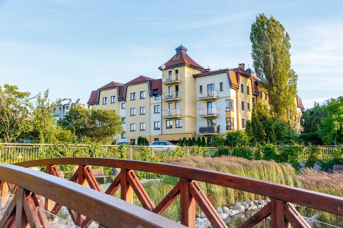 A multi-story hotel with balconies, surrounded by greenery and a wooden bridge.