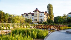 A residential building with multiple balconies, a paved pathway, and a wooden bridge over a water feature. - Apartments Happy Hours (Sopot)
