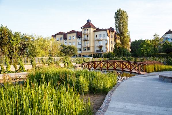 A residential building with multiple balconies, a paved pathway, and a wooden bridge over a water feature.