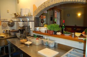 Uma cozinha com eletrodomésticos de aço inoxidável, um arco de tijolos e diversos alimentos e recipientes na bancada.