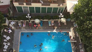 An aerial view of a swimming pool area with lounge chairs, umbrellas, and a tiled deck. - Hotel Beverly (Rimini)