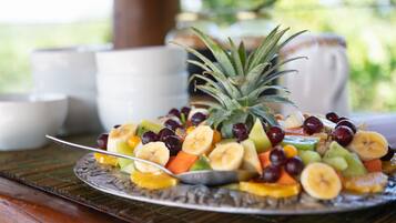 A fruit platter on a plate with a spoon, surrounded by white cups and saucers on a wooden table.