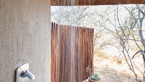 A shower with a rain-like water feature, a concrete wall, a metal faucet, and a wooden fence in the background. - Sausage Tree Safari Camp (Hoedspruit)