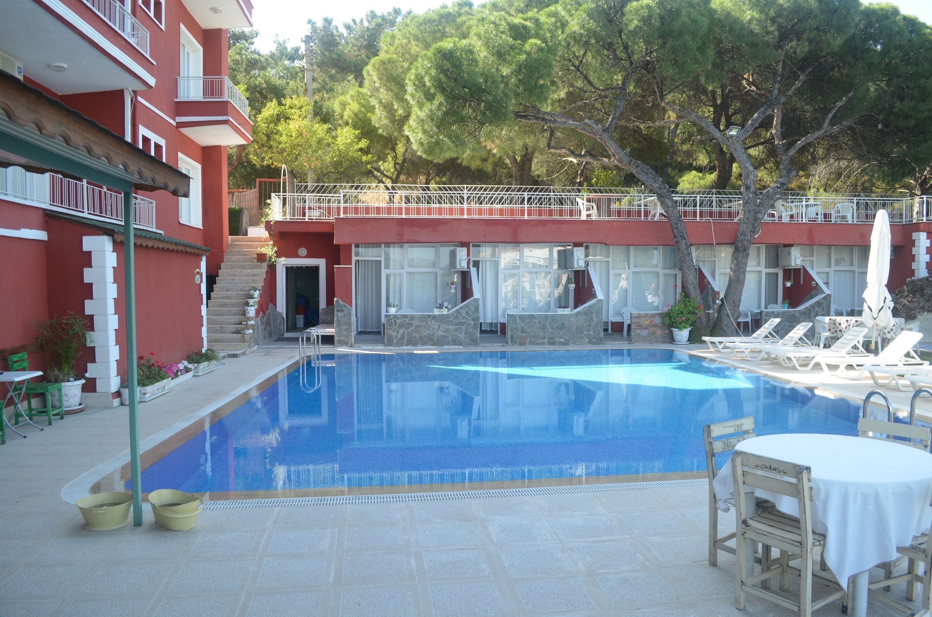 Une piscine entourée de chaises longues et d’une table, le tout bordé d’un bâtiment rouge doté de balcons et d’un escalier.