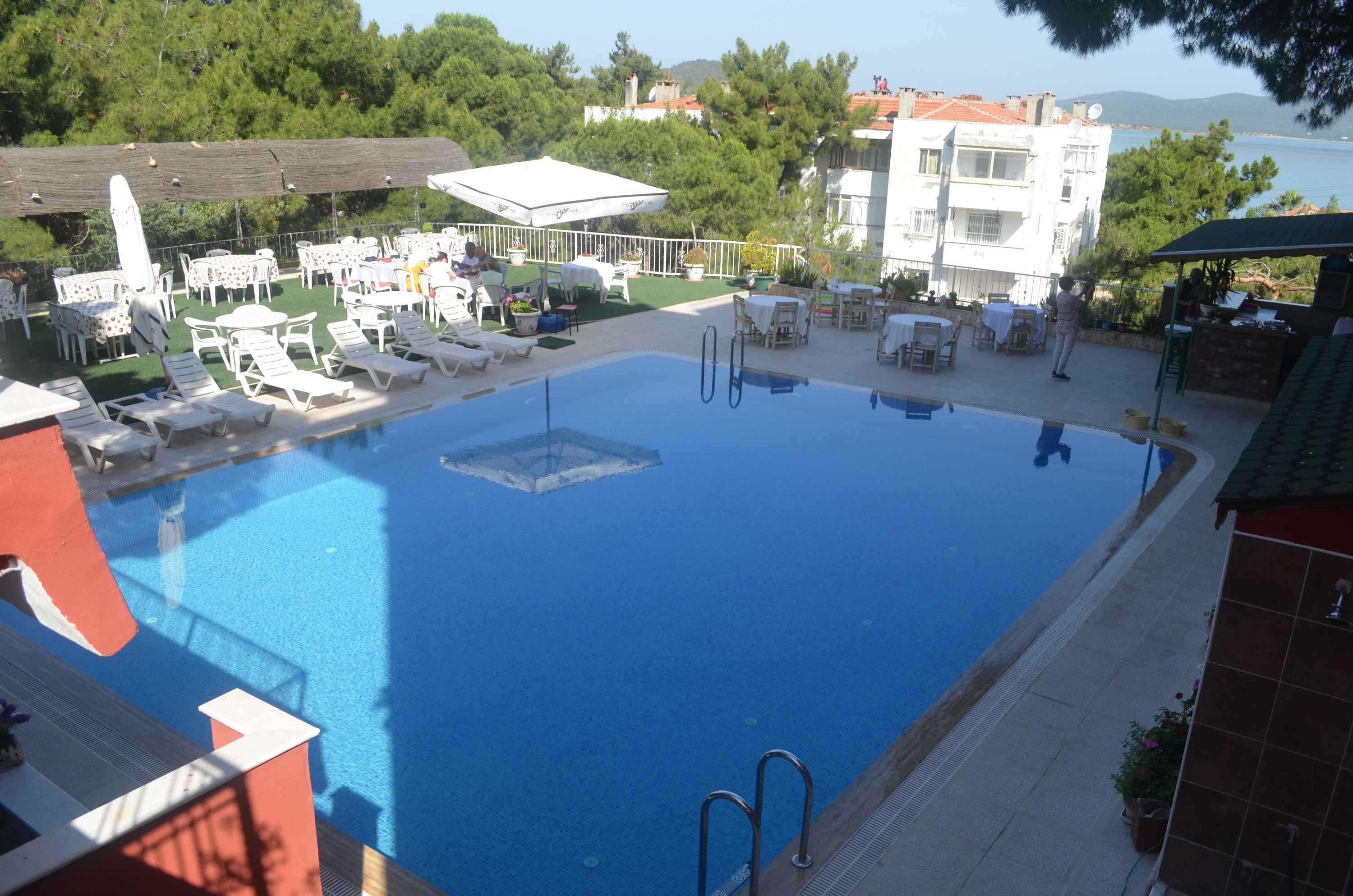 A swimming pool with lounge chairs and tables, surrounded by greenery and buildings.