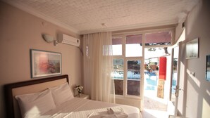 A hotel room with a bed, a window with a view of a pool, and a painting on the wall.