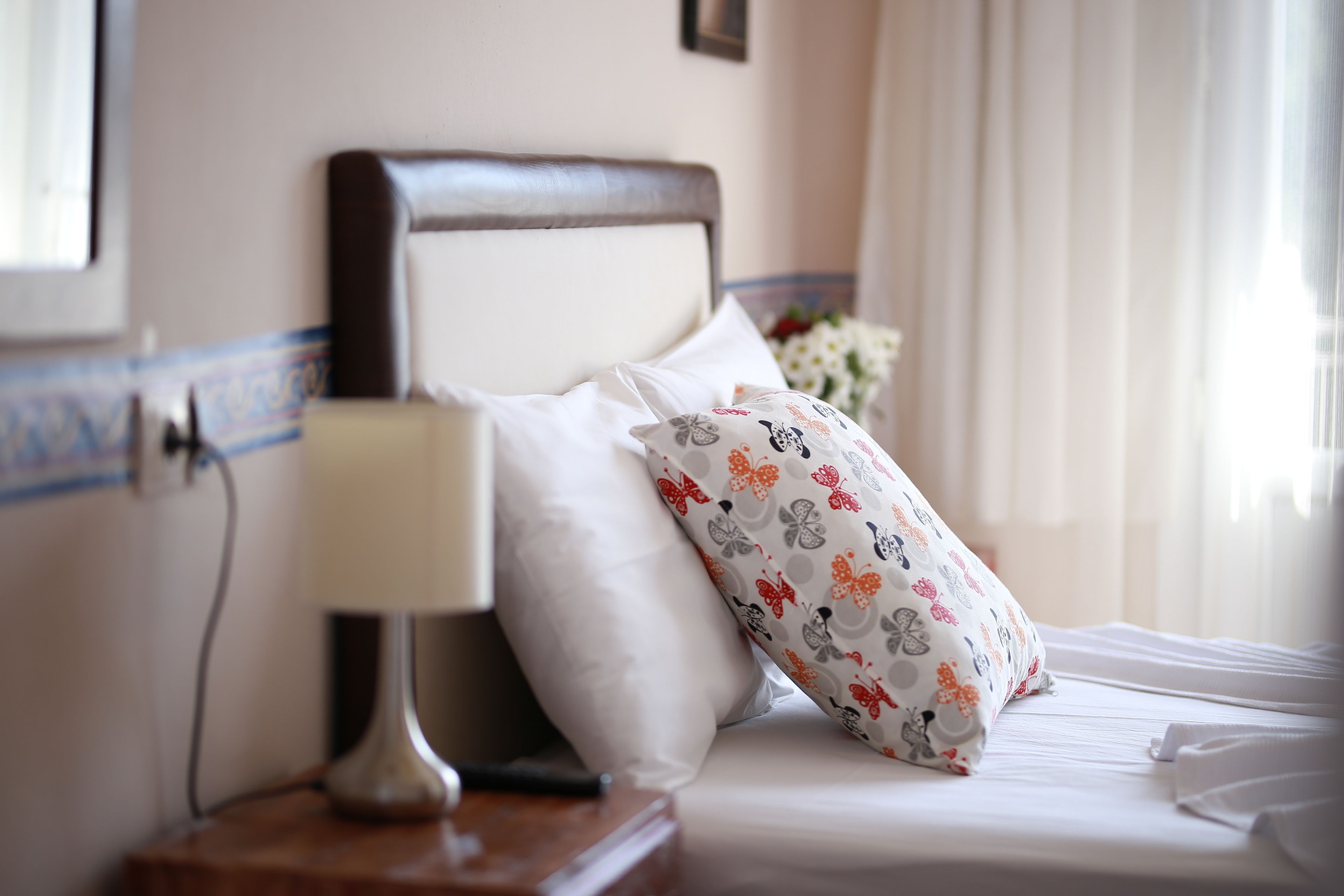 A neatly made bed with white linens and a floral-patterned pillow, a bedside lamp, and a small wooden nightstand.