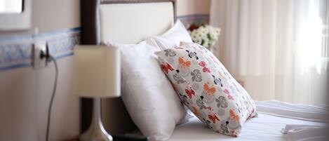 A neatly made bed with white linens and a floral-patterned pillow, a bedside lamp, and a small wooden nightstand.