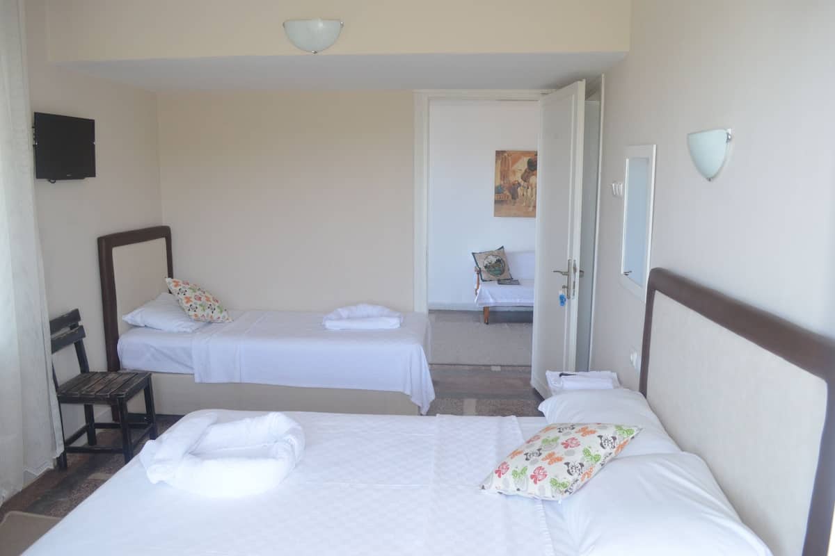 Une chambre d’hôtel avec deux lits simples, un banc en bois, une télévision et une porte donnant sur une autre pièce.