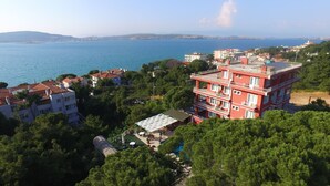 A coastal building with multiple floors, surrounded by greenery and a view of the sea.