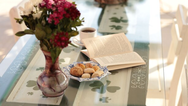 A table with a book, a cup of coffee, a plate of cookies, and a vase of flowers.
