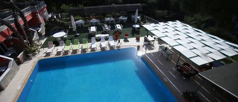A swimming pool with lounge chairs and umbrellas, surrounded by trees and buildings.