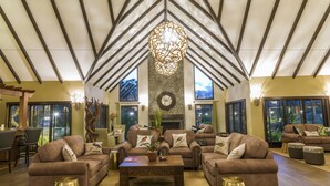 A spacious living room with a high ceiling, multiple sofas, a central coffee table, and a decorative chandelier. - The Retreat at Ngorongoro (Karatu)