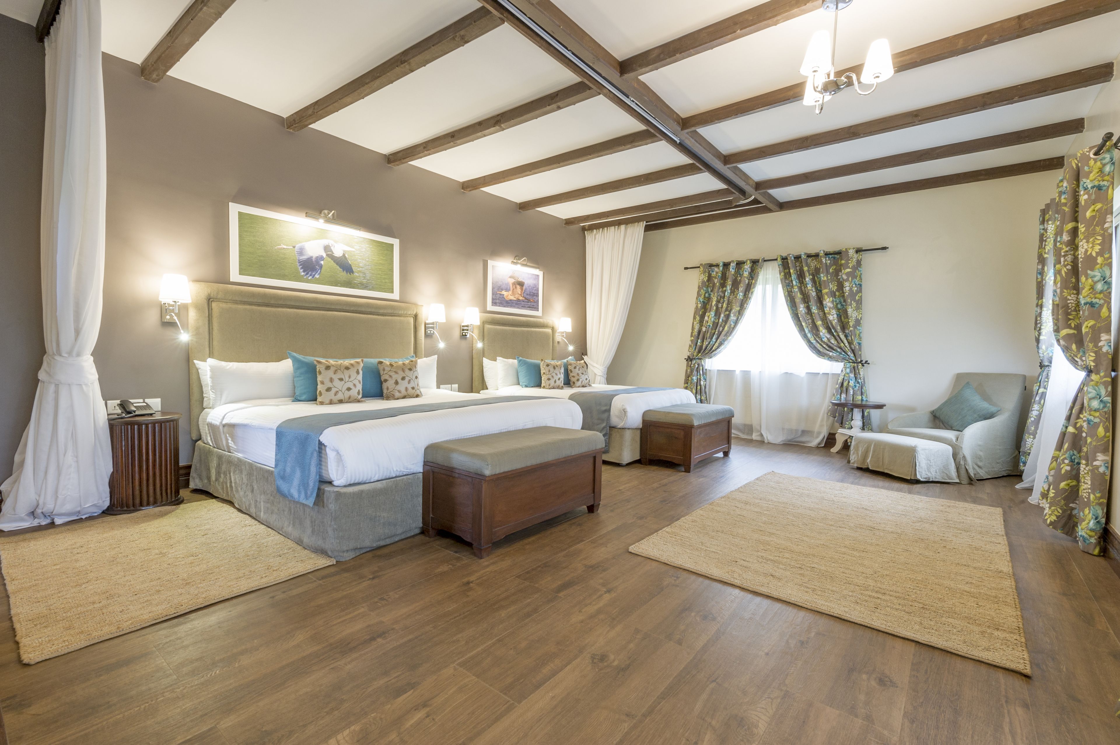 Een slaapkamer met twee bedden, houten vloeren, een groot raam met gordijnen en een kroonluchter.
