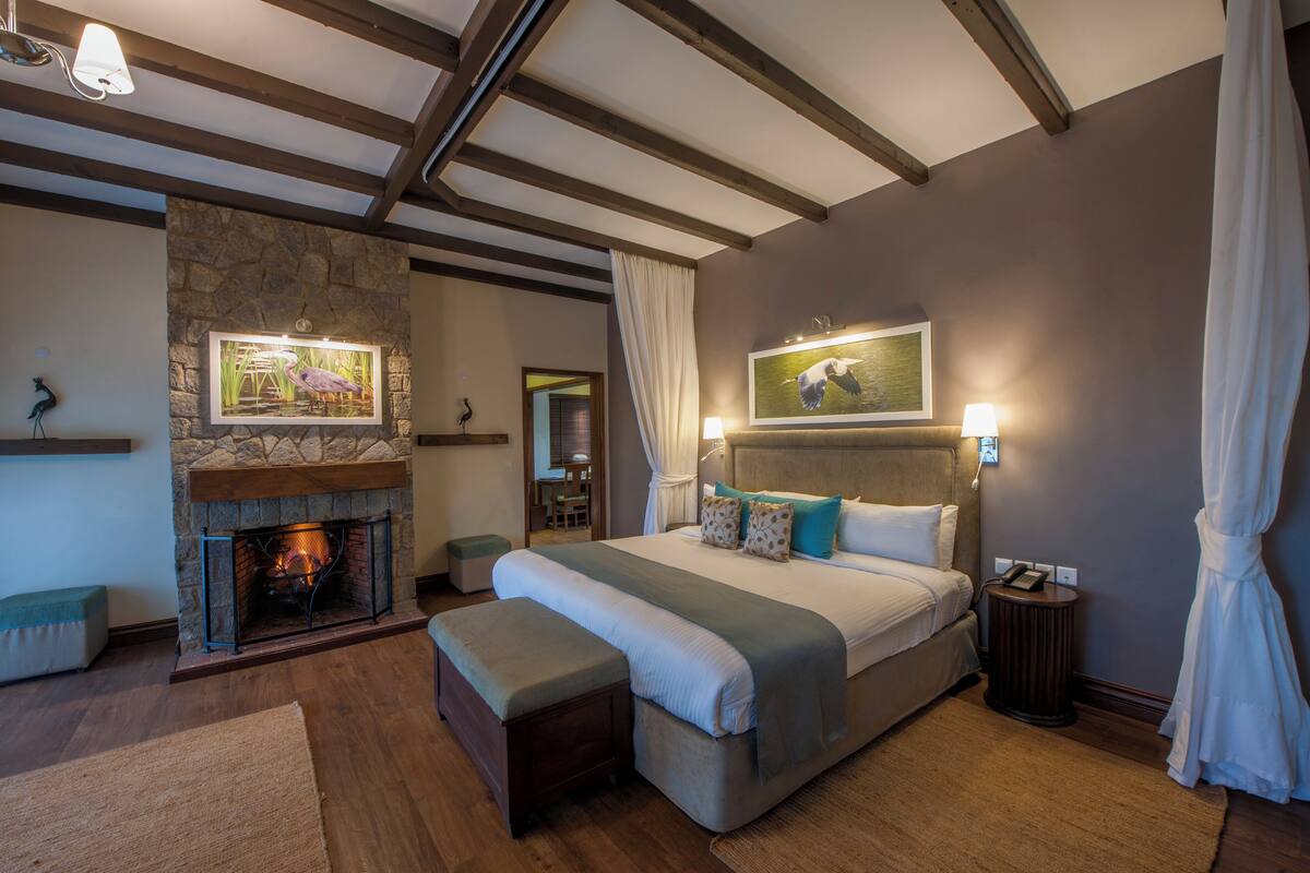 Une chambre avec une cheminée en pierre, un grand lit avec des oreillers, une table de chevet et une commode.
