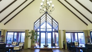 A spacious interior with a high ceiling, a central staircase, and large windows offering a view of the outdoors. - The Retreat at Ngorongoro (Karatu)