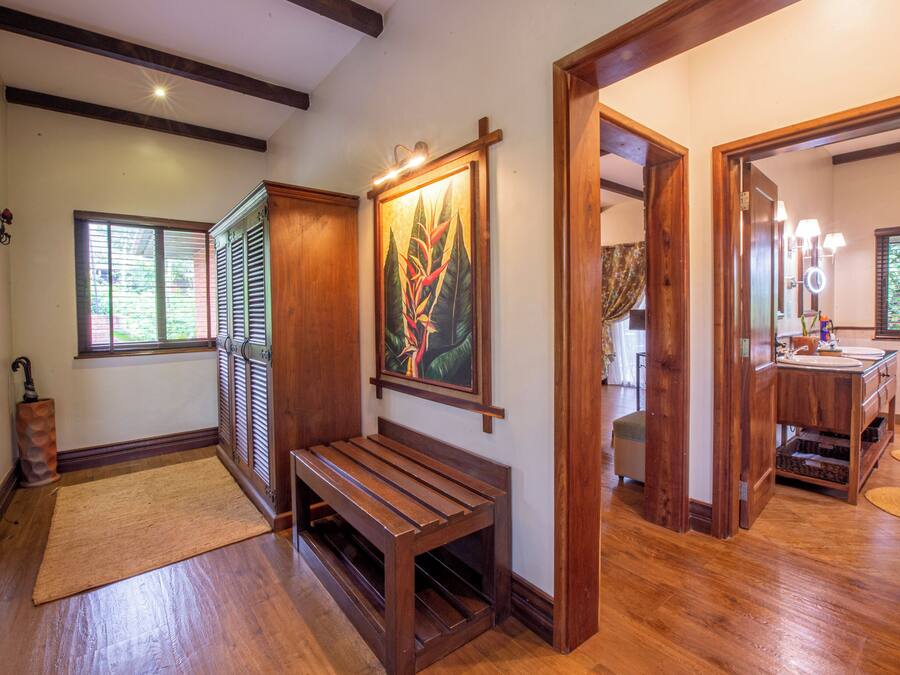 A wooden bench in a hallway with a painting above it, a radiator, and a window with blinds.
