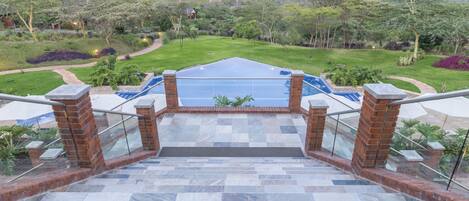 Vista desde un balcón sobre una piscina, con una escalera de piedra que baja hacia la zona de la piscina.
