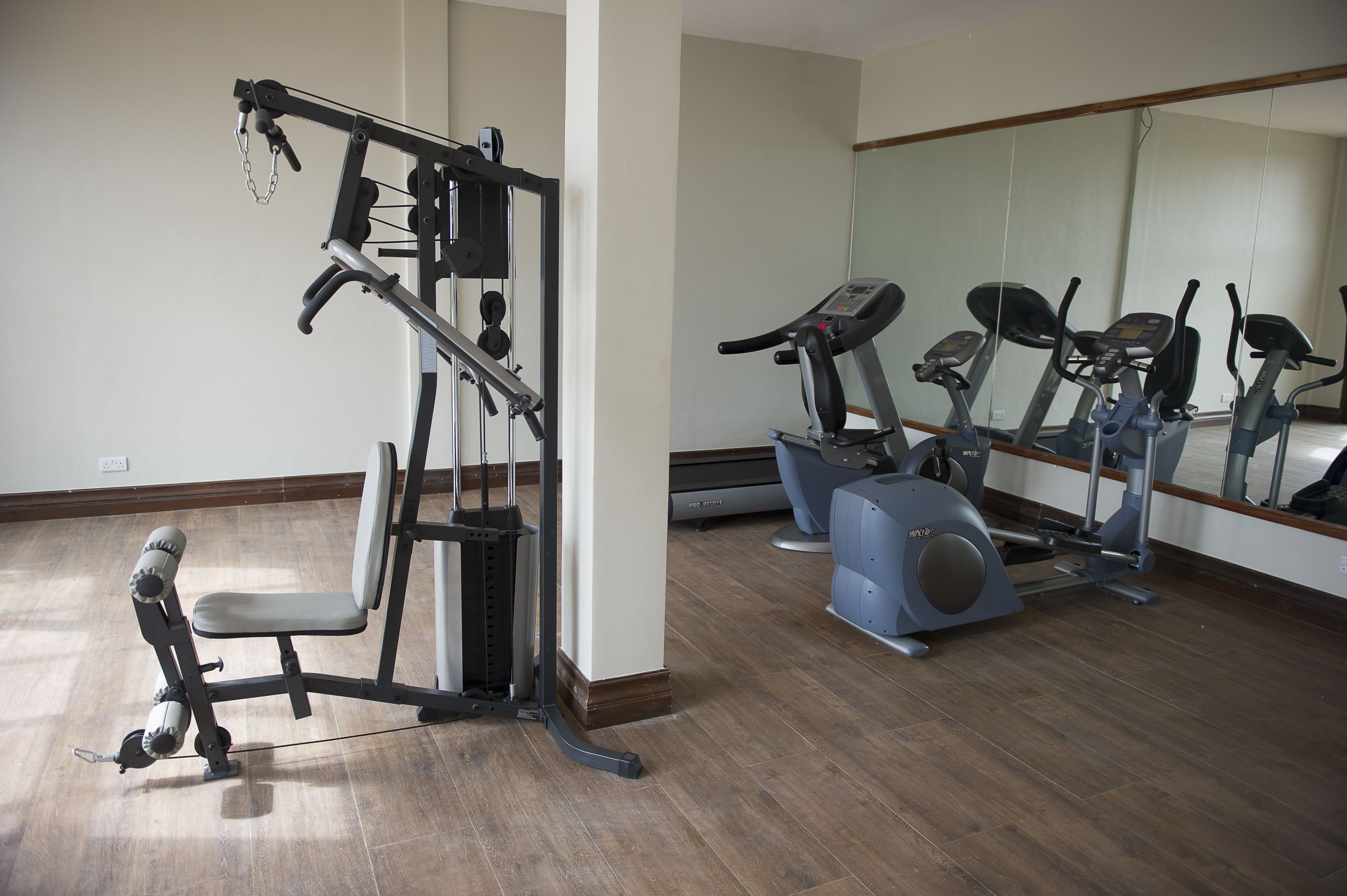 Un gimnasio con equipamiento de ejercicio, incluyendo una banca, una máquina de pesas y máquinas de cardio.