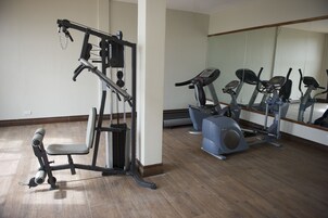 Un gimnasio con equipamiento de ejercicio, incluyendo una banca, una máquina de pesas y máquinas de cardio.