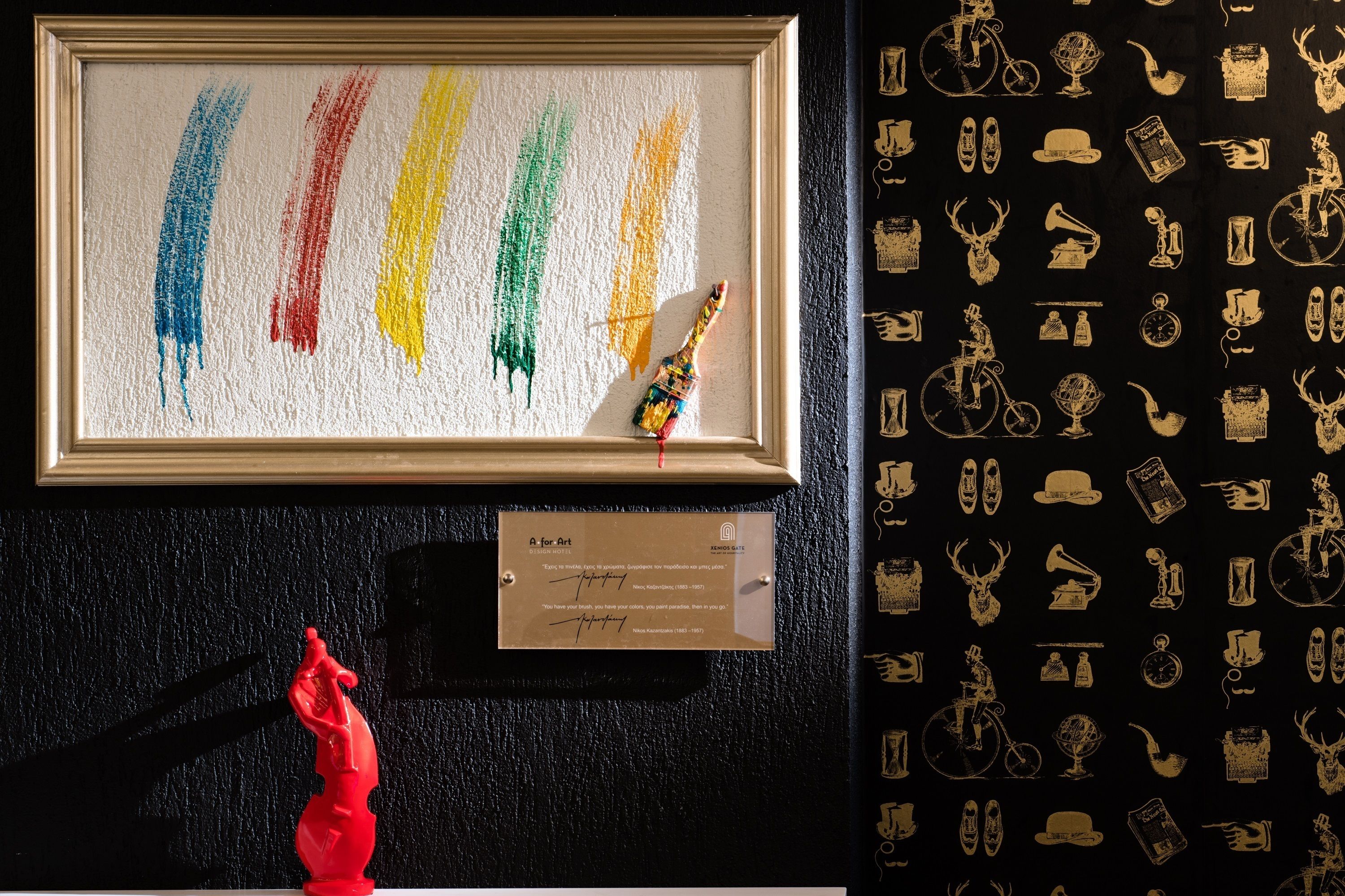 Una obra de arte enmarcada con pinceladas coloridas y una pequeña escultura, una placa con texto y una pared con iconos decorativos.