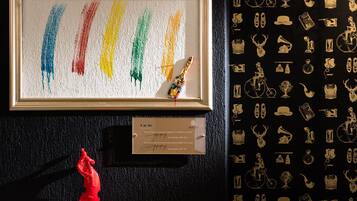 Una obra de arte enmarcada con pinceladas coloridas y una pequeña escultura, una placa con texto y una pared con iconos decorativos.