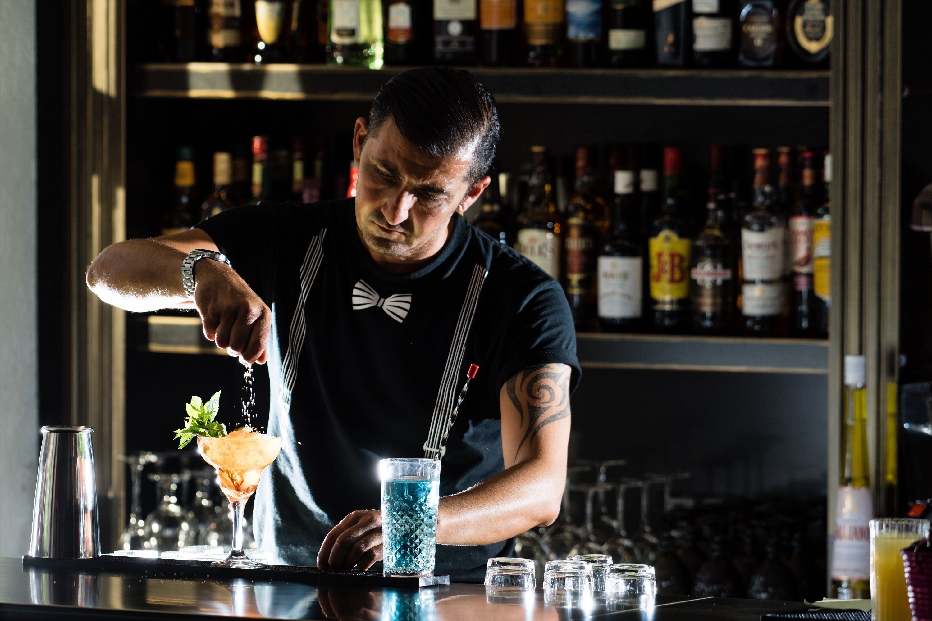 Um bartender preparando uma bebida com um agitador e um copo de cocktail no balcão.