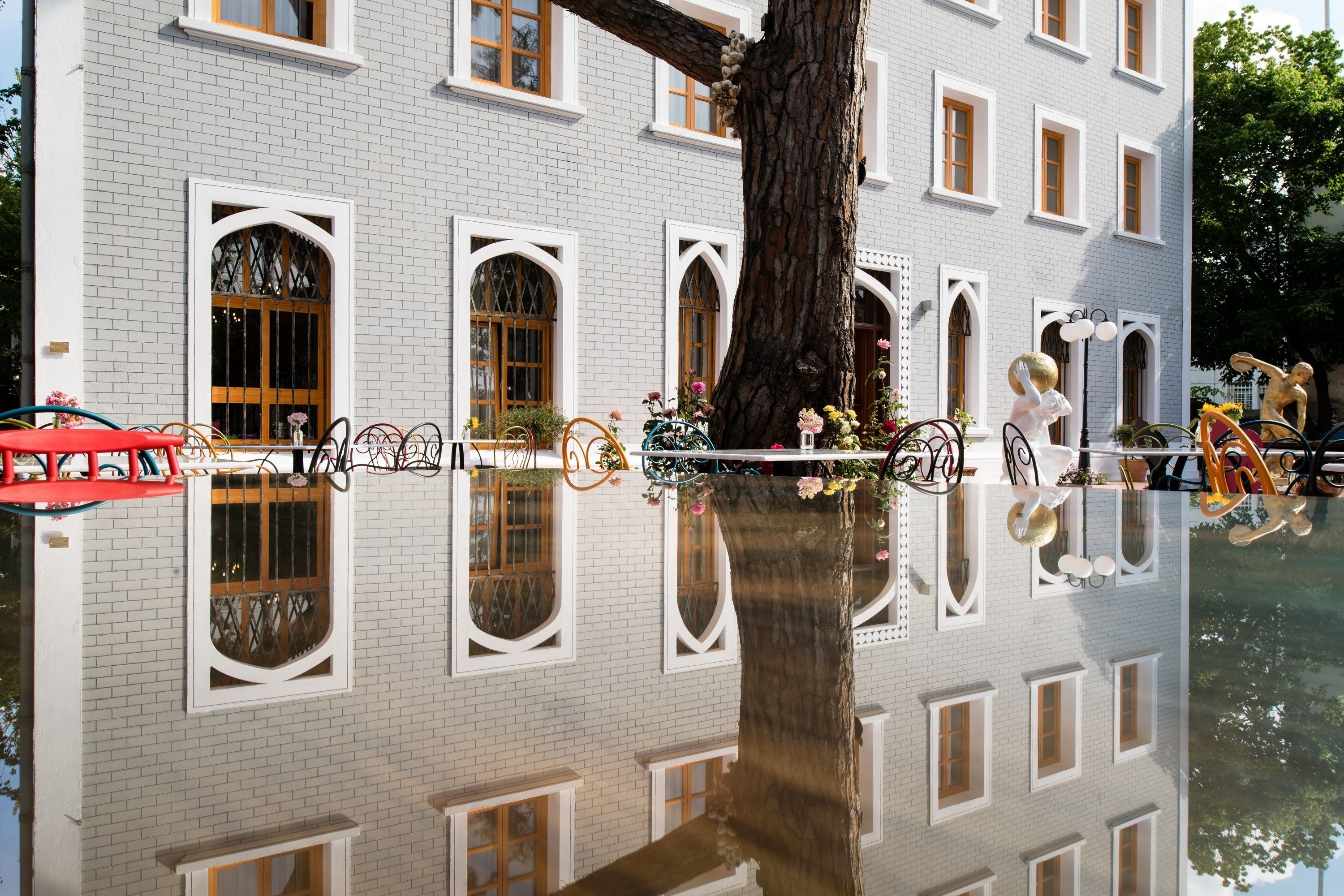 A building with white brick walls, multiple windows, and a large tree in front. - A for Art Design Hotel (Thasos)