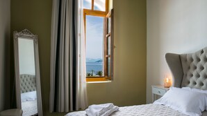 A bedroom with a bed, a nightstand with a lamp, a mirror, and a window with a view of the sea. - A for Art Design Hotel (Thasos)