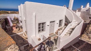 A white building with a staircase leading to a door, a small table with items on it, and a view of the sea in the background. - Skyline Villa (Santorini)