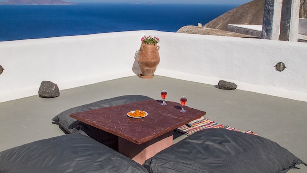 A terrace with a table, two glasses, a vase with flowers, and a view of the sea. - Skyline Villa (Santorini)