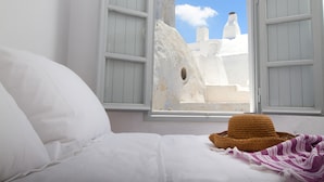 A bed with white linens, a straw hat, and a purple and white striped blanket. - Skyline Villa (Santorini)