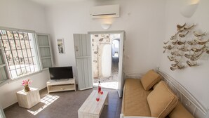 A living room with a TV, a sofa, a coffee table, and a window with blinds. - Skyline Villa (Santorini)