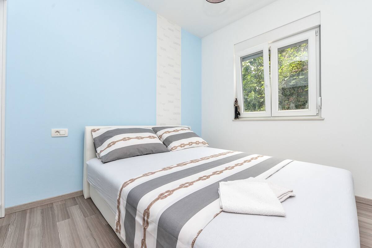 Un dormitorio con cama, ventana con vista a la vegetación y un interruptor de luz en la pared.