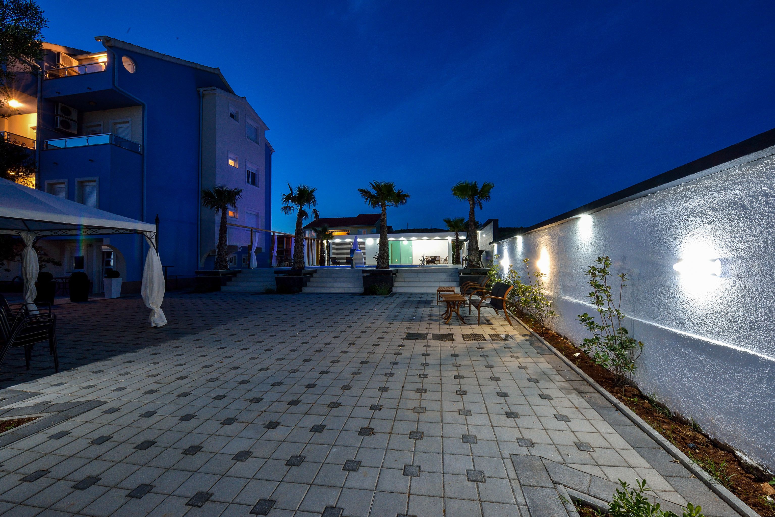 A paved courtyard with seating, palm trees, and a building with illuminated windows.