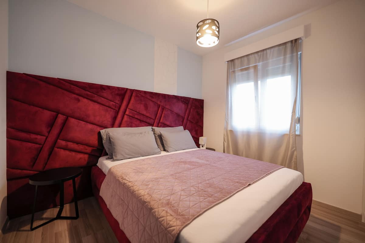 Un dormitorio moderno con una cama grande, una mesita de noche pequeña y un llamativo cabecero rojo.