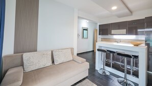 Een moderne woonkamer met een beige bank, een keuken met donkere kastjes en een bar met een barkruk.