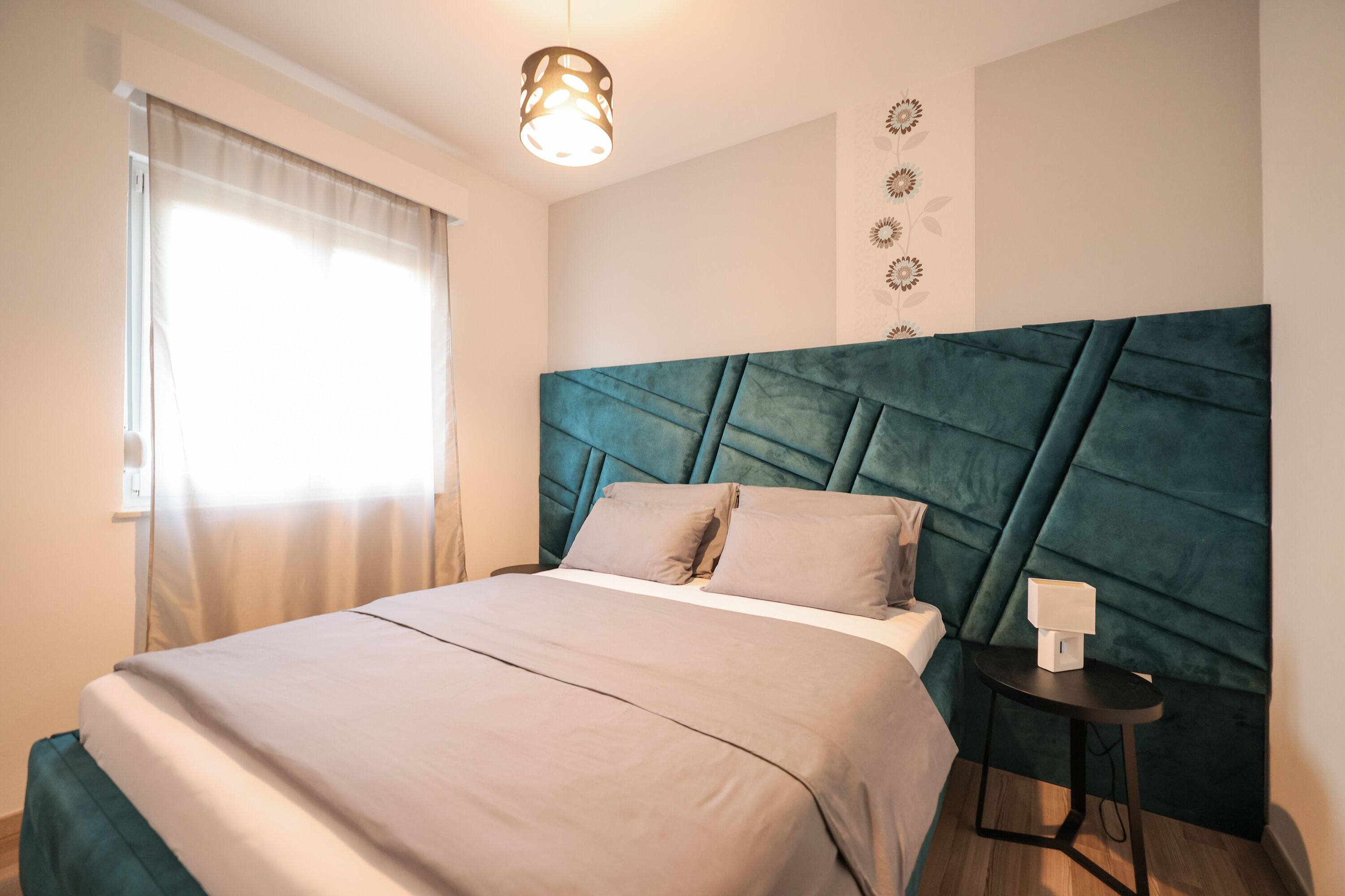 A bedroom with a large bed, a headboard, a bedside table, and a wall-mounted light fixture.
