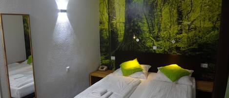 A hotel room with a bed, a nightstand, a mirror, and a forest-themed wall mural.
