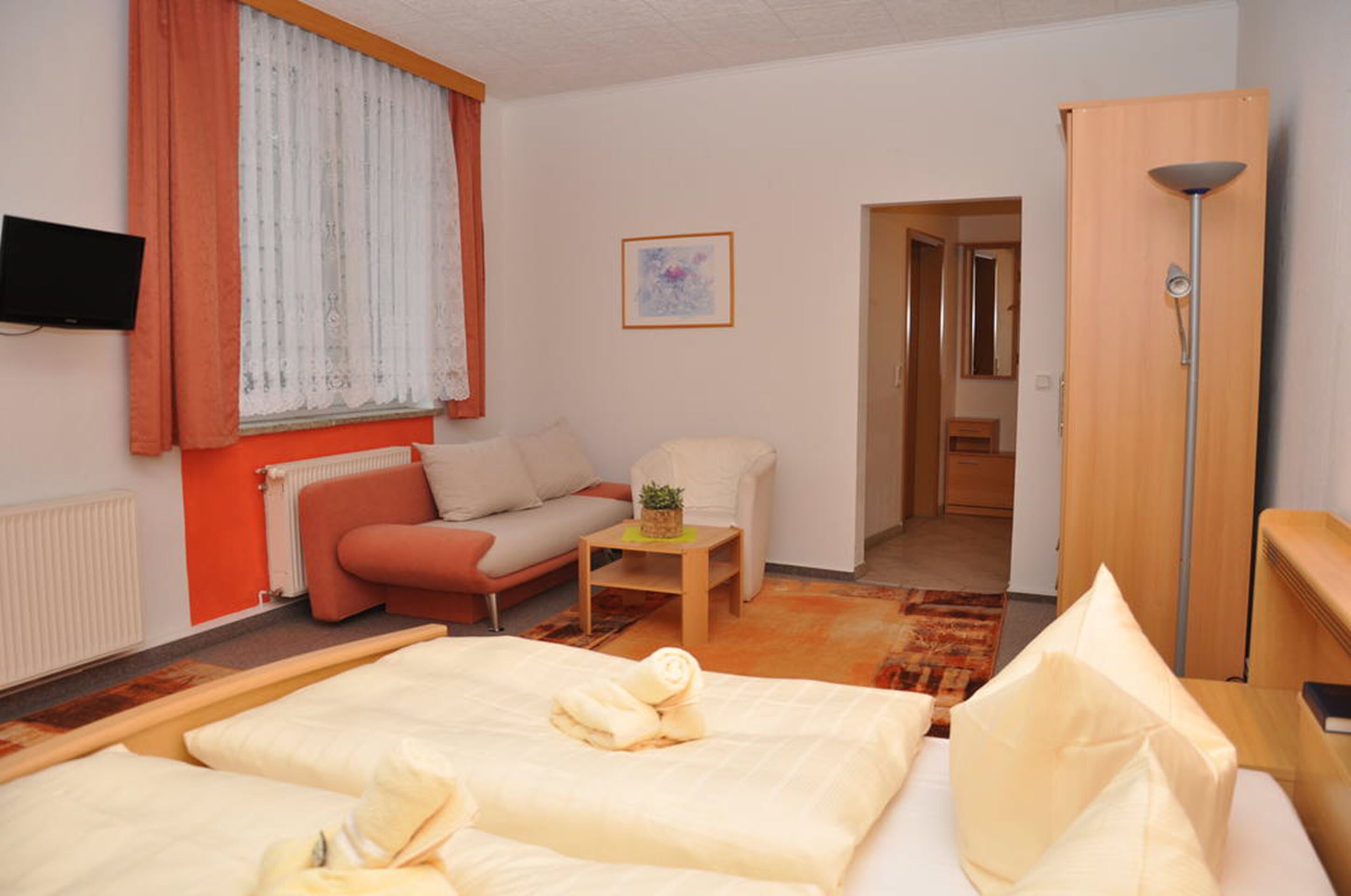 Ein Hotelzimmer mit Bett, Sofa, kleinem Tisch, Fernseher und Kleiderschrank.